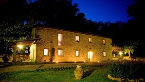A stone building with multiple windows, a garden with a large vase, and outdoor lighting. - VILLA LIZ, private pool, private hot tub, park fenced,  close to Florence (Poppi)