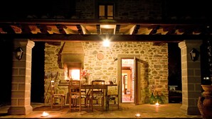 A stone building with a covered patio, a table with chairs, and a lit fire. - VILLA LIZ, private pool, private hot tub, park fenced,  close to Florence (Poppi)