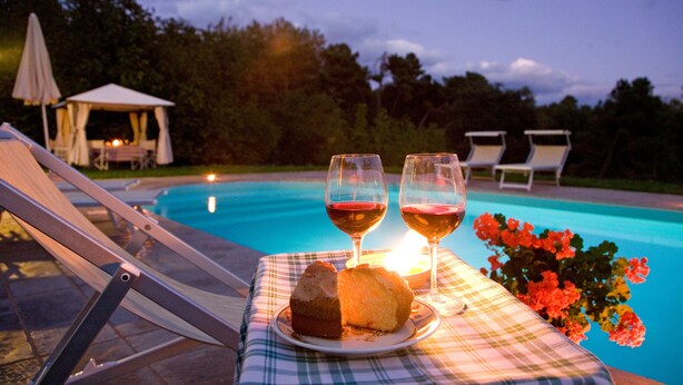A poolside table with a plate of food and two glasses of red wine, surrounded by lounge chairs and a gazebo. - VILLA LIZ, private pool, private hot tub, park fenced,  close to Florence (Poppi)