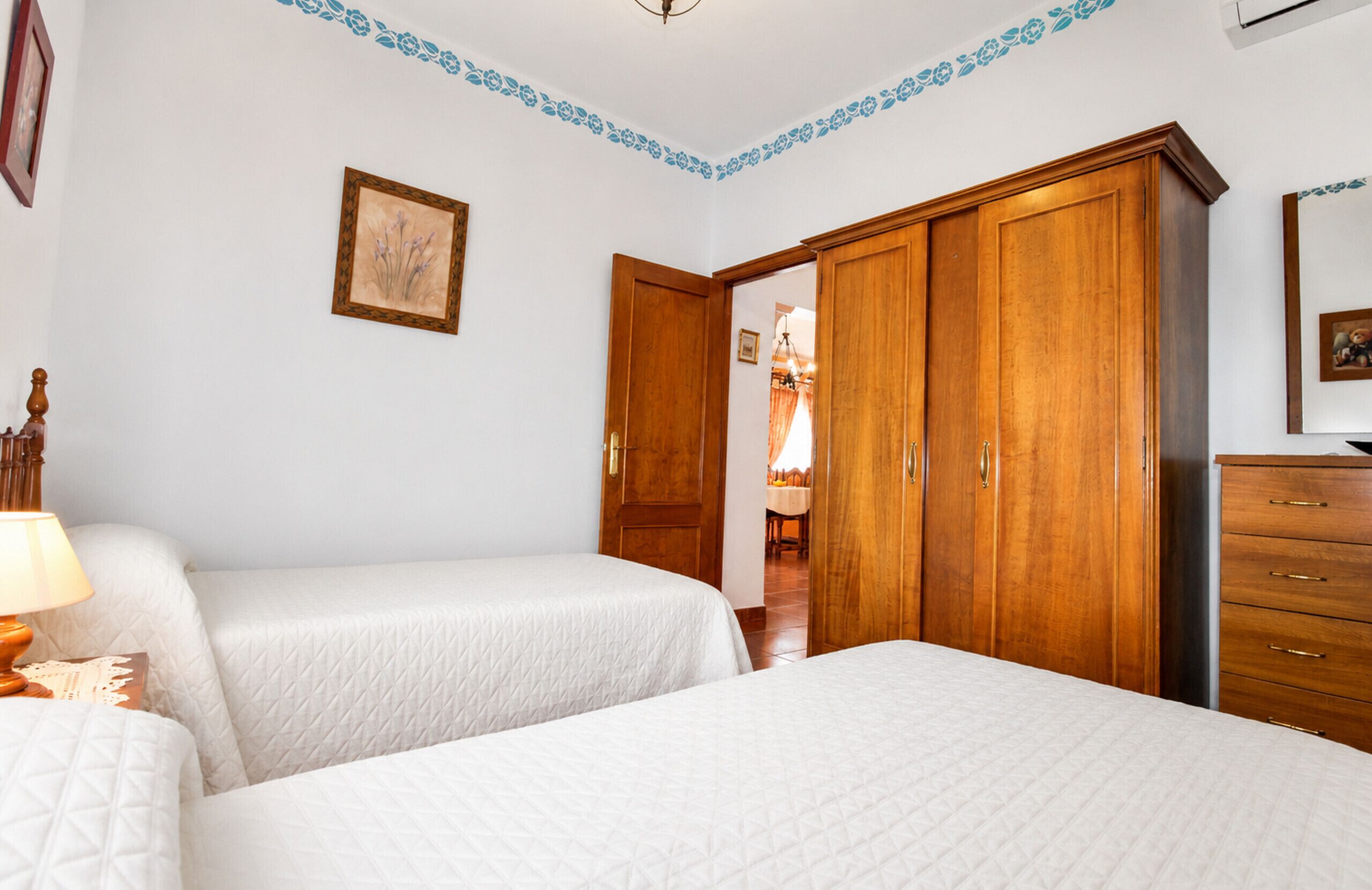 Ein Schlafzimmer mit zwei Betten, einem Holzschrank, einem Nachttisch und einem gerahmten Bild an der Wand.