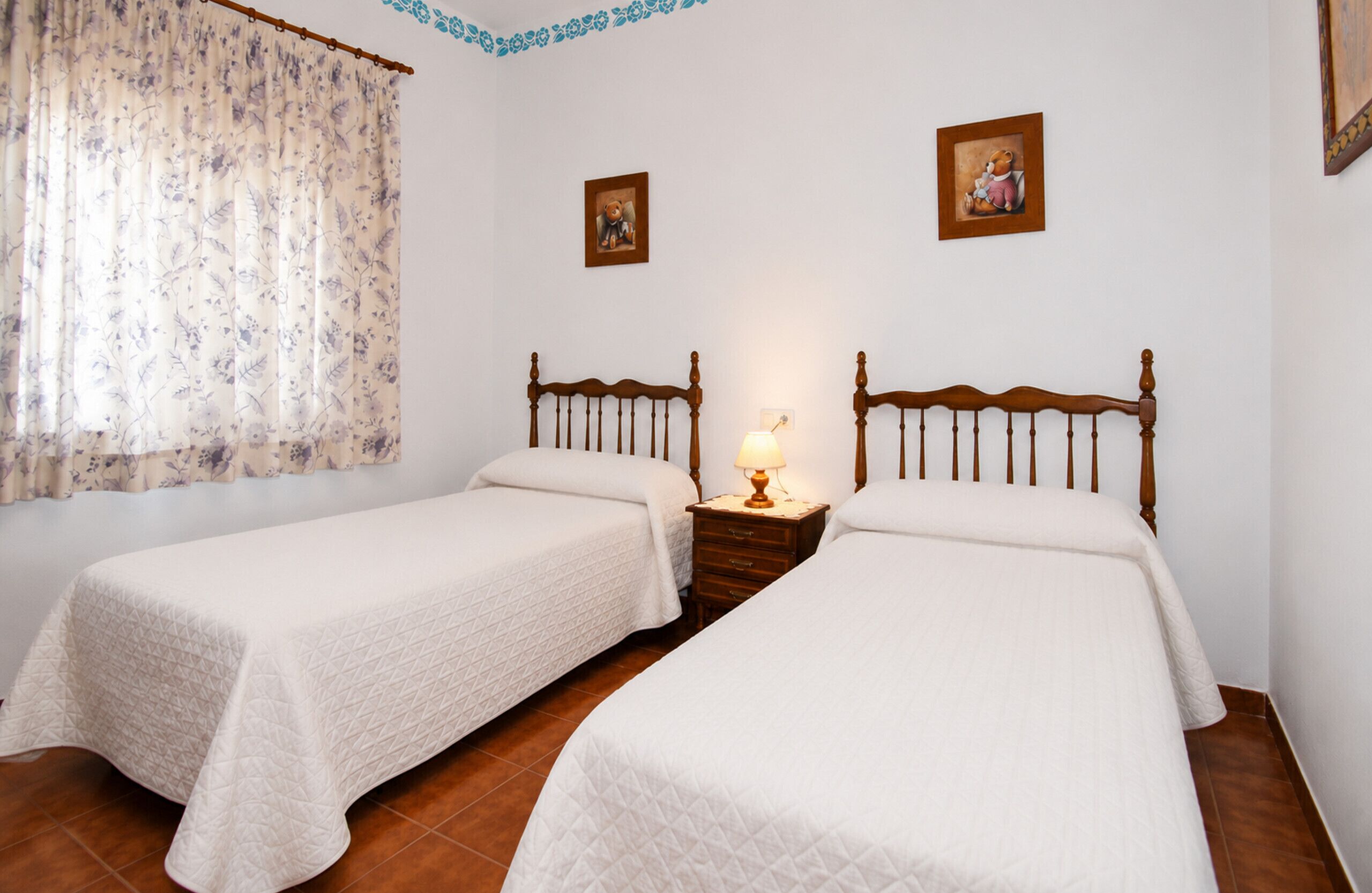 A double room with two beds, a nightstand with a lamp, and two framed pictures on the wall.