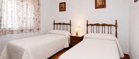 A double room with two beds, a nightstand with a lamp, and two framed pictures on the wall.