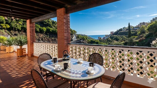 Un espace extérieur aménagé, abrité et doté d’une table pour deux, entouré de chaises, et offrant une vue panoramique sur une colline verdoyante.