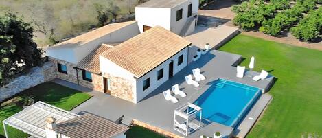 A modern house with a swimming pool, a covered patio, and a well-maintained lawn.
