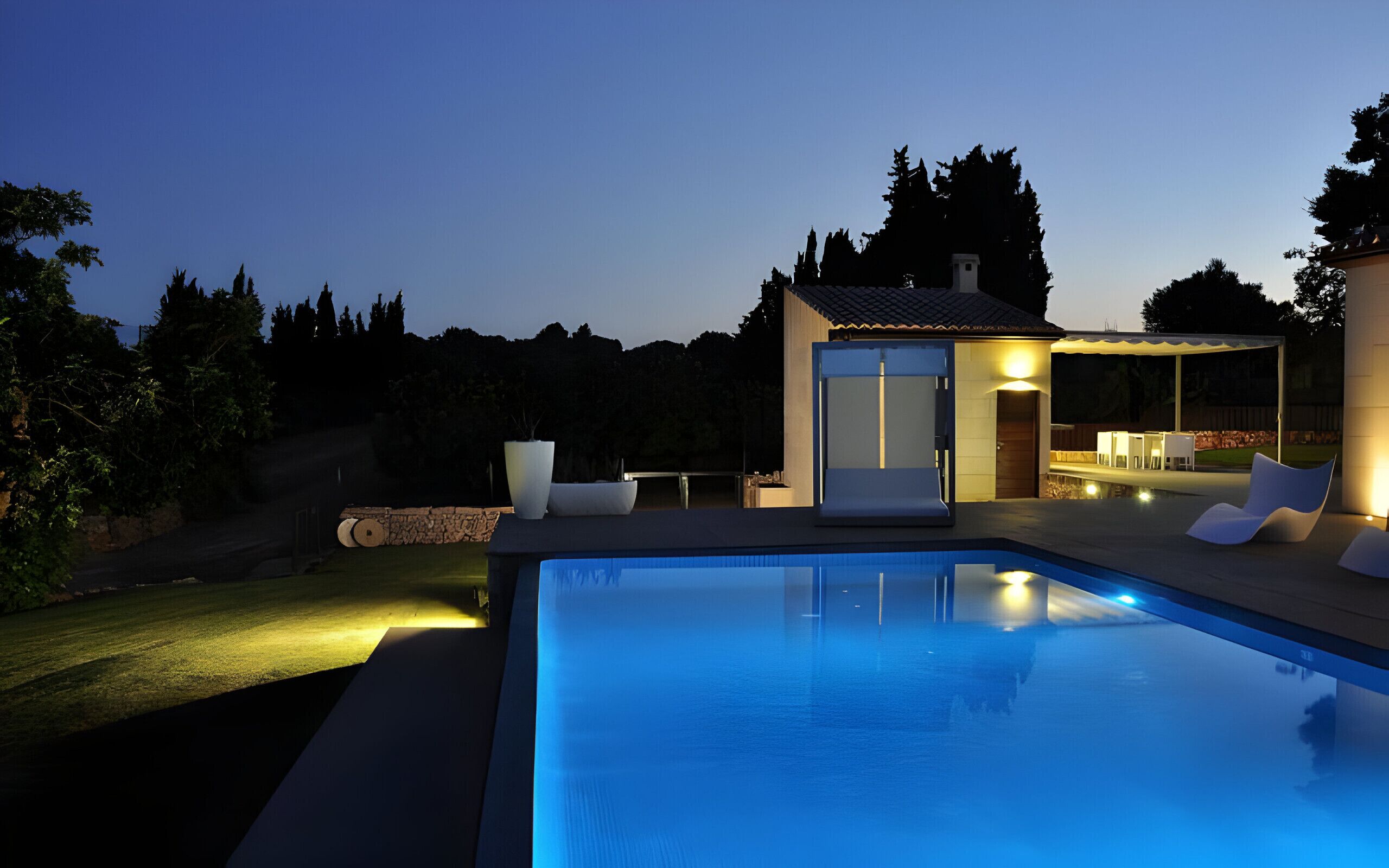 Un espace piscine extérieur moderne, doté d’une piscine à l’eau d’un bleu limpide, d’un petit espace salon couvert et d’une pelouse bien entretenue.