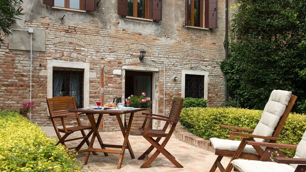 An outdoor patio with a brick wall, a table with chairs, and a hedge. - Elegant apartment with garden in S.Croce, Venice (Santa Croce)