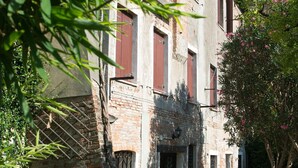 A traditional stone building with a brick facade, a central entrance, and a small garden area with a pathway leading to the entrance. - Elegant apartment with garden in S.Croce, Venice (Santa Croce)