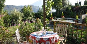 A table set outdoors with a view of mountains and a garden. - Garden apartment in the heart of the countryside, close to local villages. (Pórtugos)