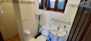 A small bathroom with a toilet, sink, and a window above the sink. - Garden apartment in the heart of the countryside, close to local villages. (Pórtugos)
