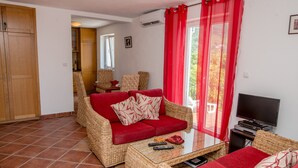 Ein Wohnzimmer mit einem roten Sofa, Korbmöbeln, einem Glastisch und einem Fernseher.