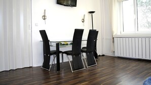 Zona pranzo con tavolo e quattro sedie, una TV a schermo piatto montata a parete, una lampada da terra e una finestra con tende.