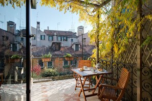Ein Balkon mit Tisch und Stühlen, Blick auf Gebäude und einem Metallzaun.