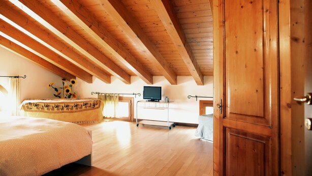 A room with wooden beams on the ceiling, a bed with a patterned bedspread, a television on a stand, and a wooden wardrobe. - CASA GIULIA in BORSO DEL GRAPPA A holiday full of sport (Borso del Grappa)