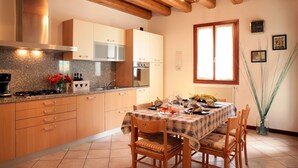 A kitchen with wooden cabinets, a granite countertop, a dining table with chairs, and a window with blinds. - CASA GIULIA in BORSO DEL GRAPPA A holiday full of sport (Borso del Grappa)