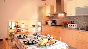 A kitchen with wooden cabinets, a microwave, and a sink. There is a dining table with a tablecloth and a fruit bowl. - CASA GIULIA in BORSO DEL GRAPPA A holiday full of sport (Borso del Grappa)