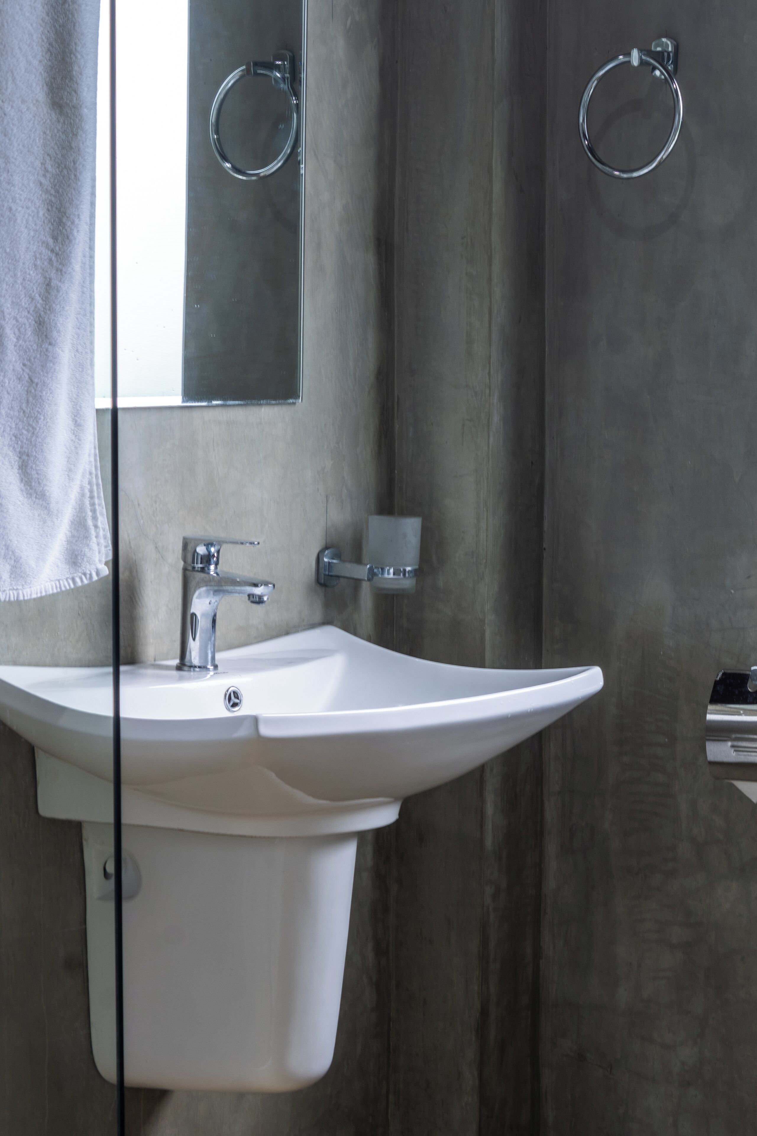 A bathroom with a white sink, chrome faucet, and a mirror. There are two towel rings on the wall.