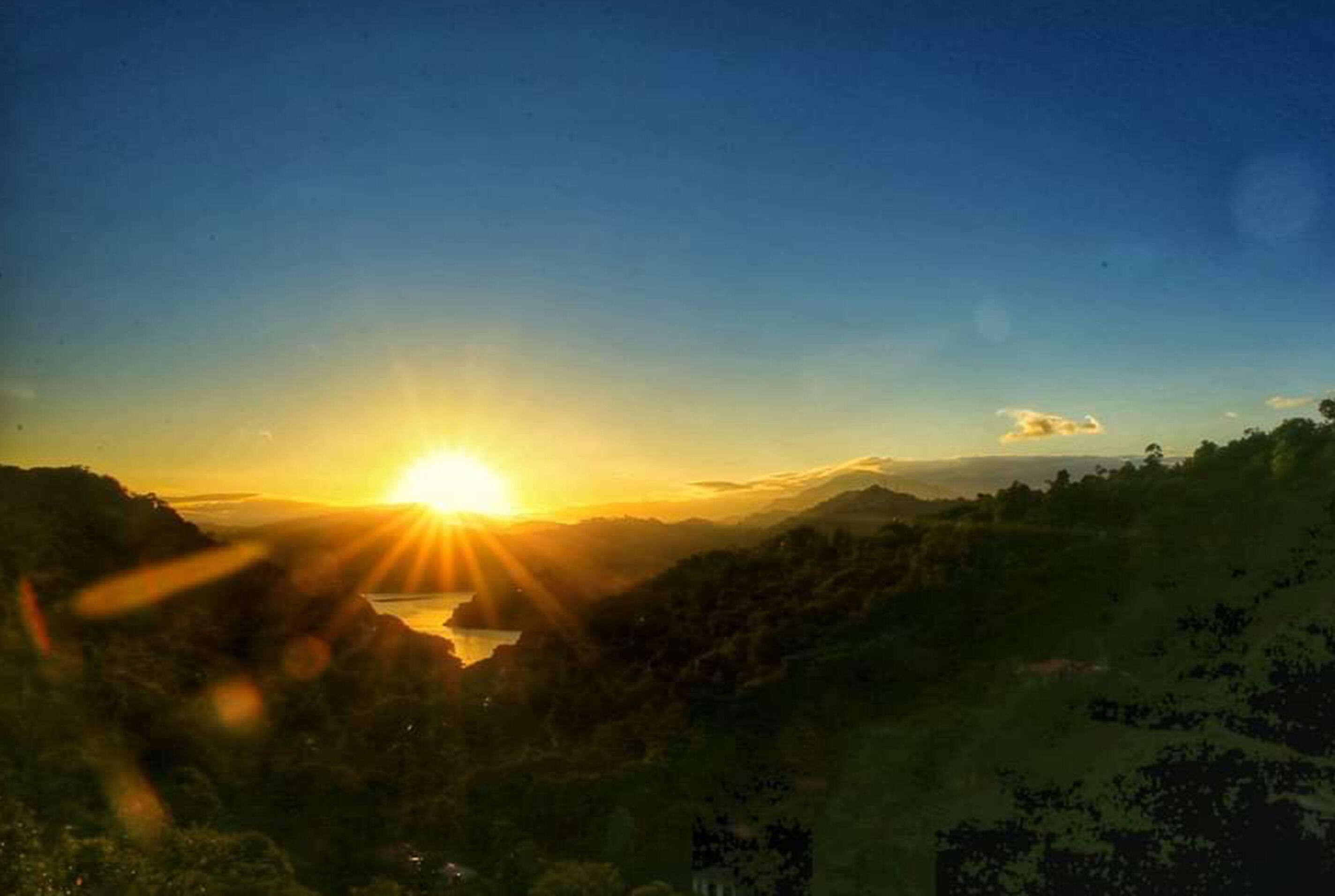 A sunset over a mountainous landscape with a body of water in the foreground.