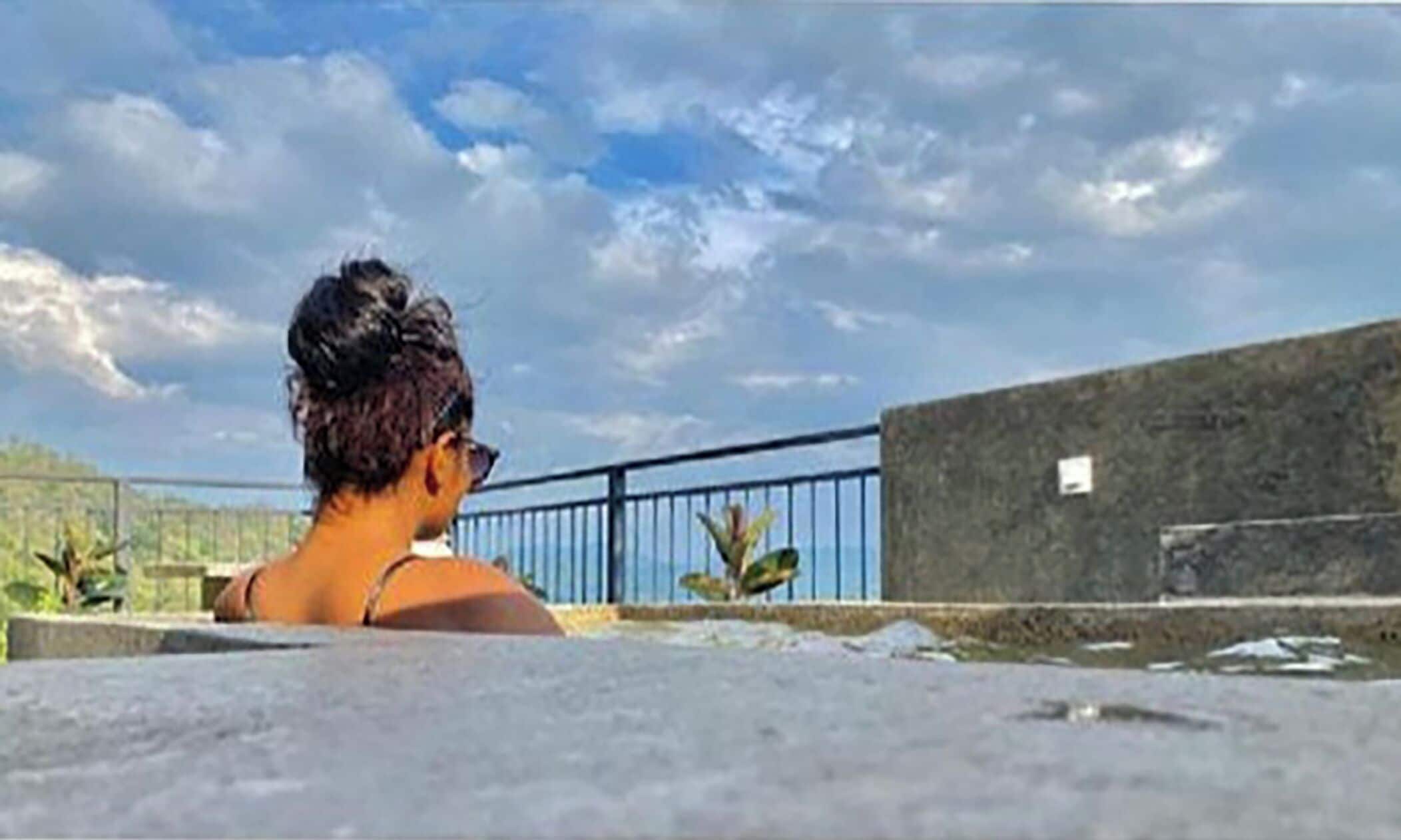 A person sitting on a concrete ledge with a view of the sky and a blue railing.