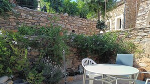 Terrassa exterior amb taula rodona i cadires, envoltada per una paret de pedra i vegetació exuberanta.