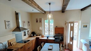 Una cuina amb armaris de fusta, una taula de dinar amb caires, un fogó i una finestra amb cortines.