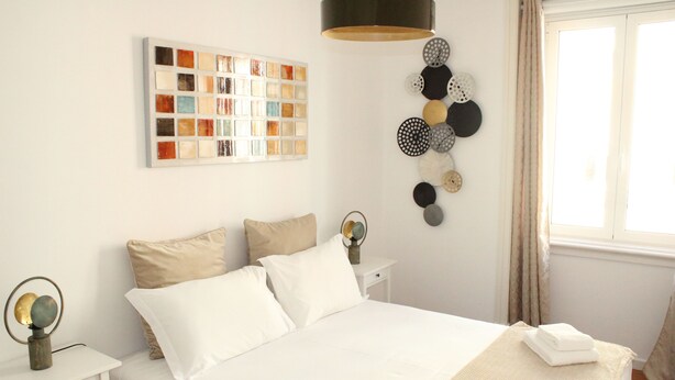 A neatly arranged hotel room with a bed, a bedside table, a wall art piece, and a decorative wall hanging.