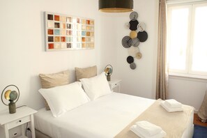 A neatly arranged hotel room with a bed, a bedside table, a wall art piece, and a decorative wall hanging.