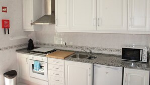 A kitchen with white cabinets, a stainless steel range hood, a microwave, a sink, and a wooden cutting board.