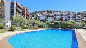 A swimming pool with a clear blue water, surrounded by a paved area, and adjacent to multi-story residential buildings.