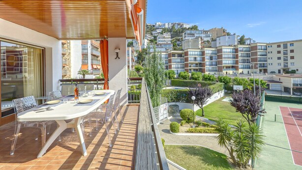 A balcony with a table and chairs, a view of a residential area, and a tennis court.