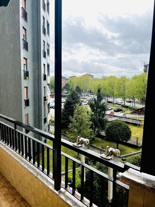 A balcony with a view of a residential area, including a multi-story building and a park with trees and parked cars.