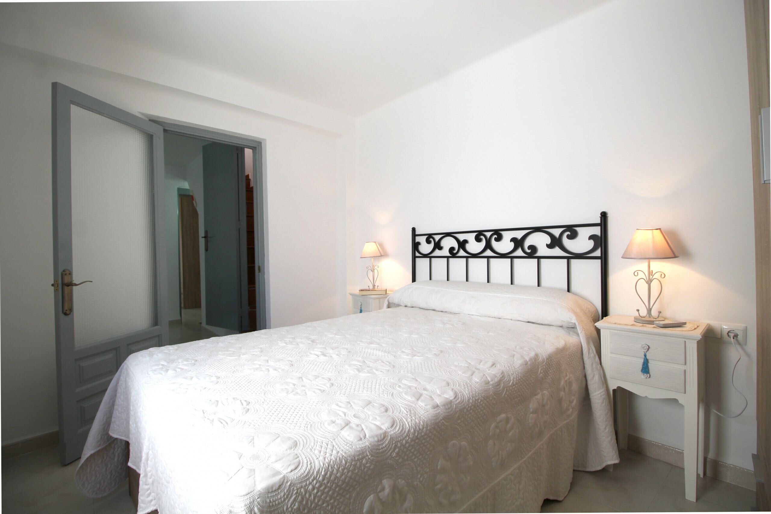 A bedroom with a bed, two bedside tables with lamps, a door, and a wall-mounted light fixture.