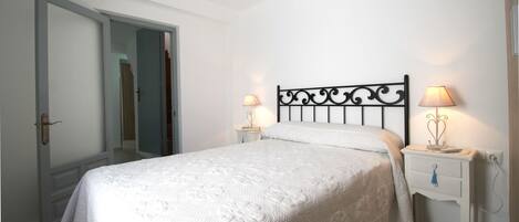 A bedroom with a bed, two bedside tables with lamps, a door, and a wall-mounted light fixture.