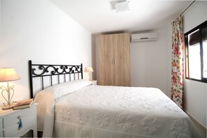 A bedroom with a bed, a nightstand with a lamp, a wardrobe, and a window with curtains. - 1050 Casa Carretas (Nerja)