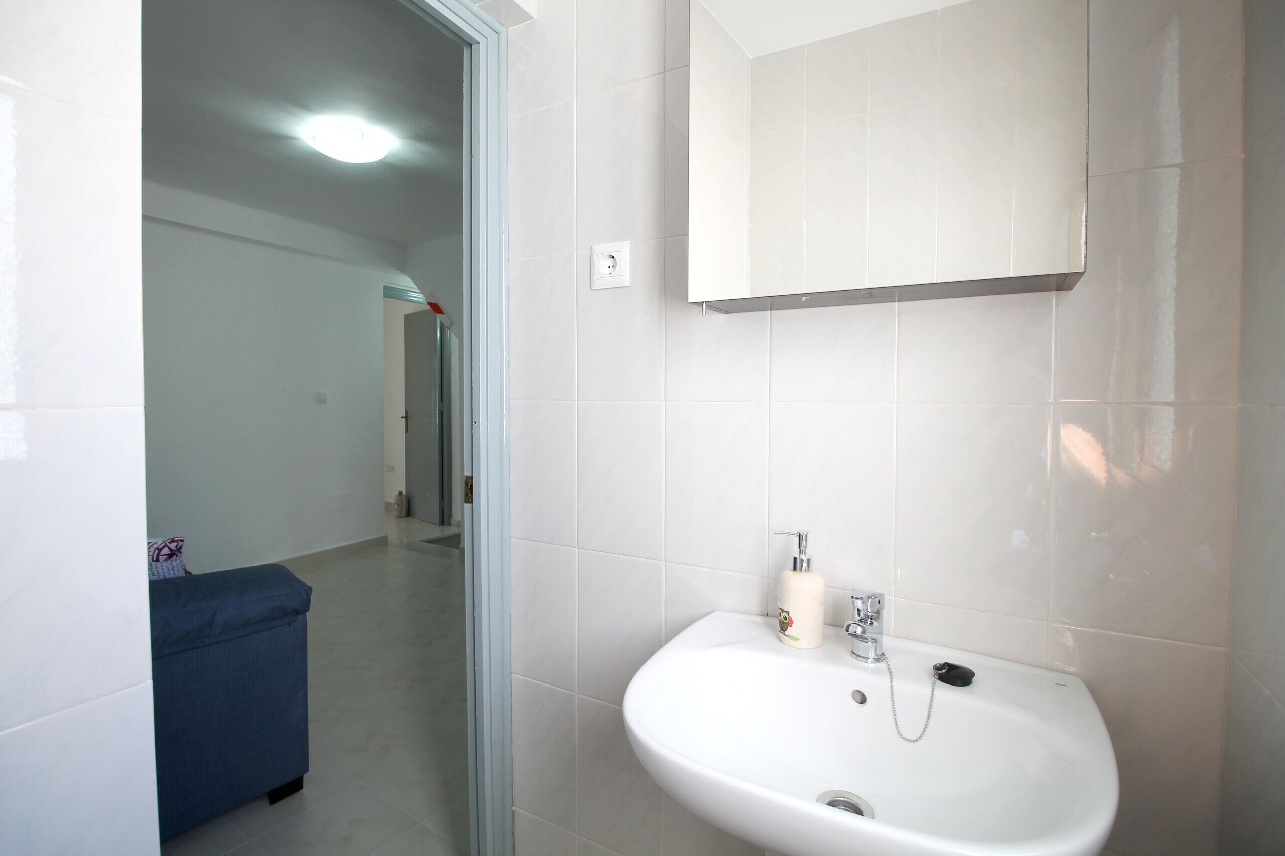 A bathroom with a white sink, a mirror, and a blue bench.