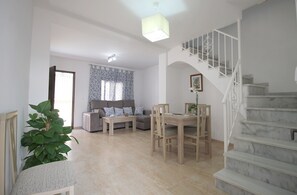 A spacious living area with a sofa set, a dining table, and a staircase. - 1050 Casa Carretas (Nerja)