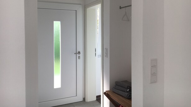 Un pasillo con una puerta blanca, un banco de madera y un estante con toallas dobladas.