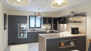 A modern kitchen with dark cabinets, a central island, a built-in oven, and a coffee machine. - Villa with pool for discerning connoisseurs (Bagnols en foret)