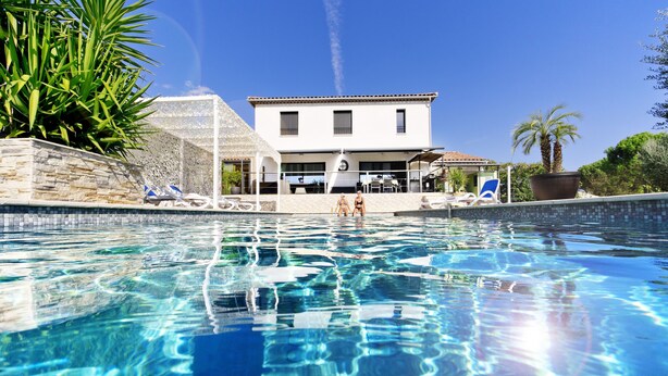 A swimming pool with clear blue water, lounge chairs, and a building with a tiled roof in the background. - Villa with pool for discerning connoisseurs (Bagnols en foret)
