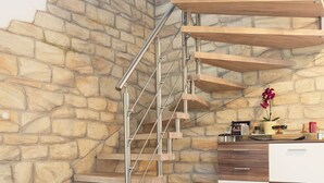 A modern staircase with a stone wall backdrop, a wooden chest, and a kitchen area with a stone countertop. - Villa with pool for discerning connoisseurs (Bagnols en foret)