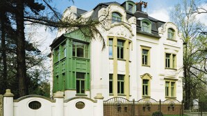 A large, ornate building with a white facade, green window shutters, and a brick base.