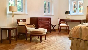 A bedroom with wooden flooring, a dresser, two chairs, a desk, and a lamp.