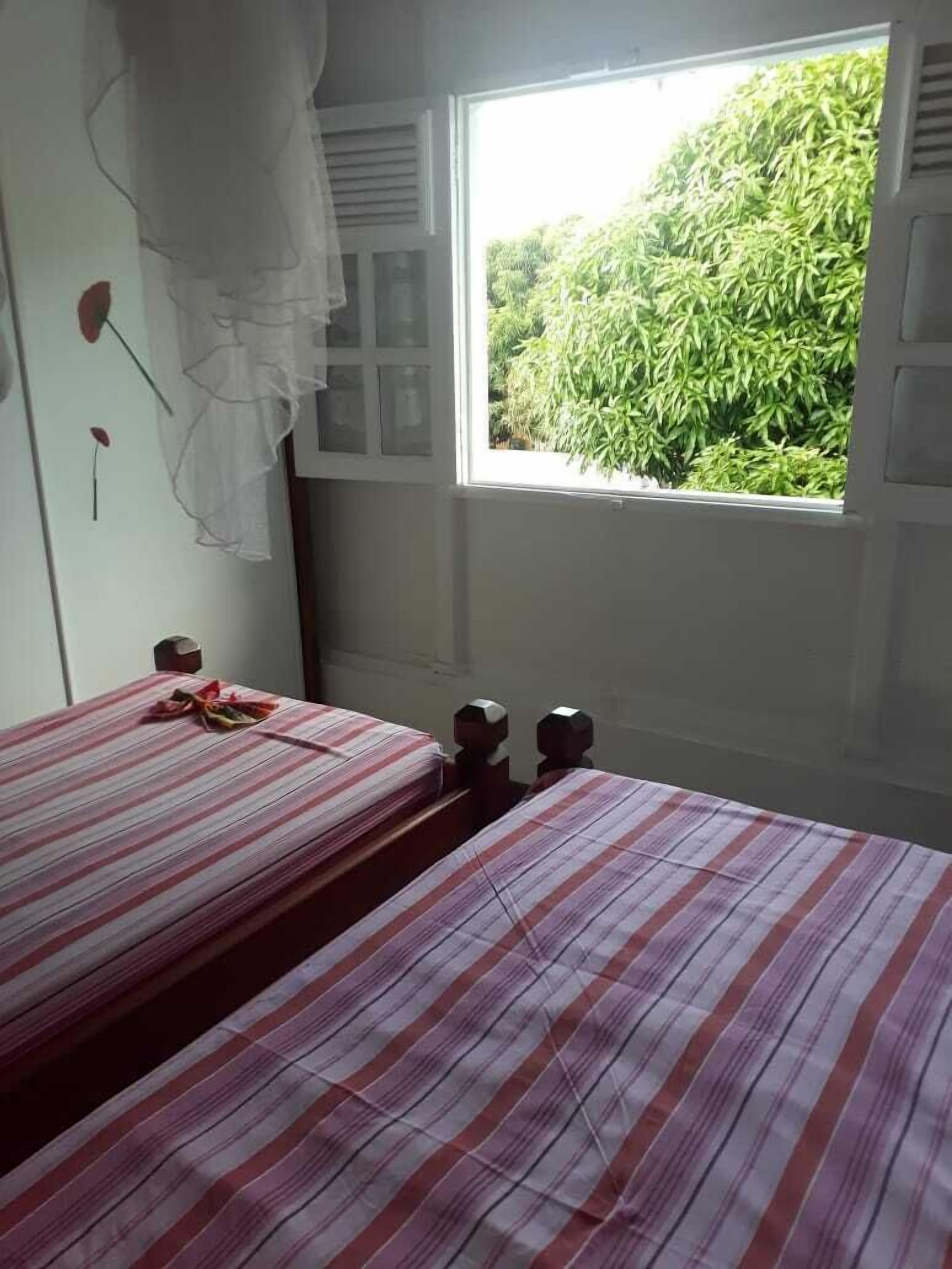 A room with two beds, a window with a view of greenery, and a wall with a decorative item.