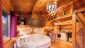 A cozy cabin interior with a round bed, wooden walls, a kitchen area, and a large window with curtains. - House with garden in the center of Berlin for up to 3 people (Berlin)