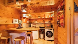 A compact kitchen with wooden walls, a washing machine, and a small bar area with stools. - House with garden in the center of Berlin for up to 3 people (Berlin)