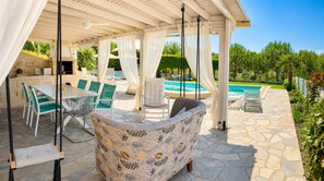 A covered outdoor seating area with stone flooring, a pool, and a patio with chairs and a table. - Villa Alina in Haniotis with private pool (Chaniotis)