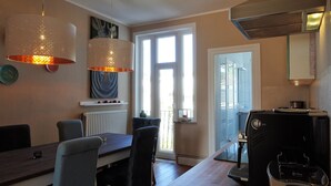 Un coin repas avec une table et des chaises en bois, un radiateur et un espace cuisine équipé d’un grille-pain.