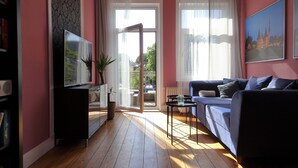 Un salon avec un téléviseur, un canapé et une grande fenêtre avec des rideaux.