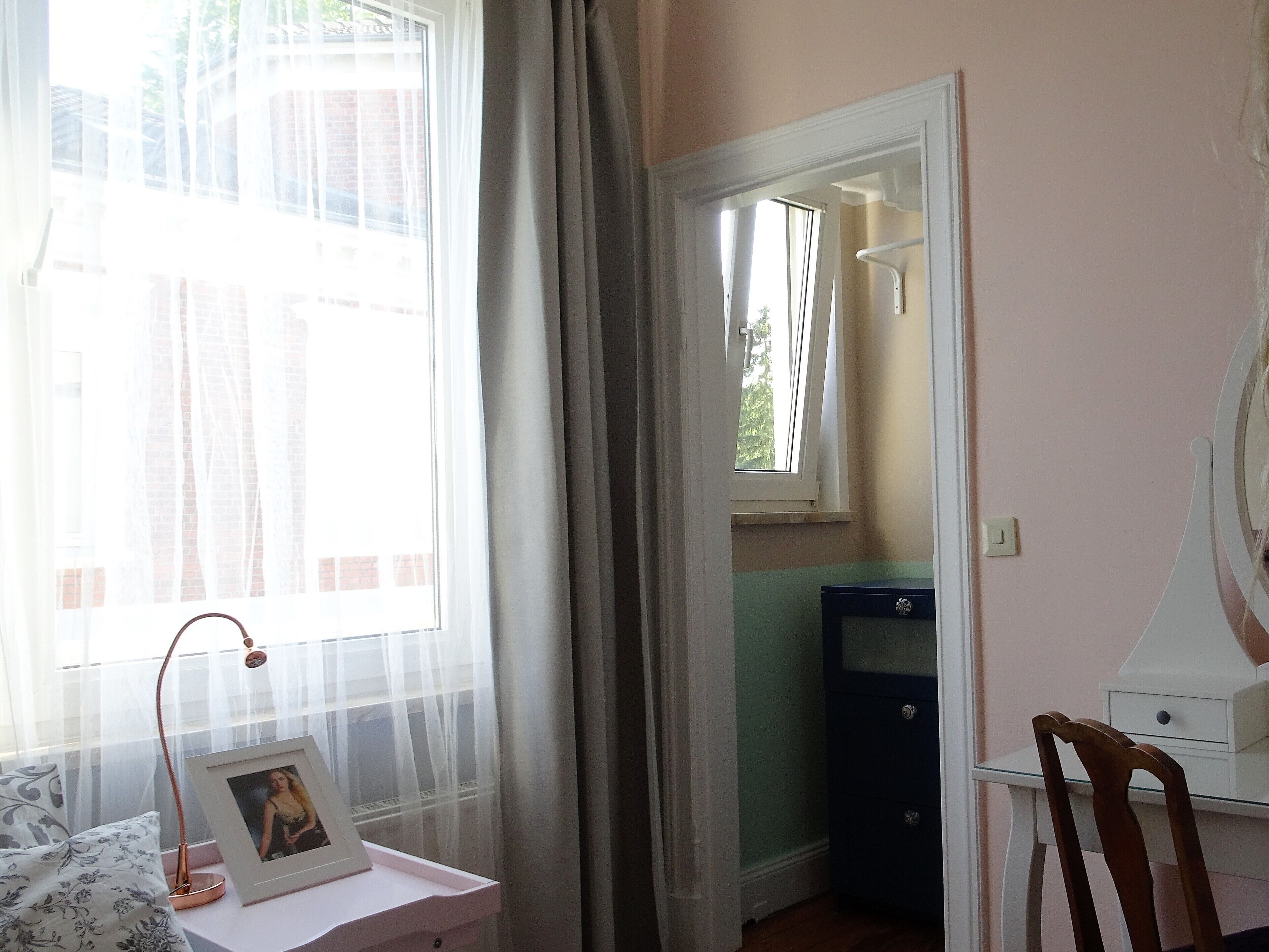 Una stanza con un letto, un comodino con lampada e una cornice, una scrivania con una sedia e una finestra con tende.