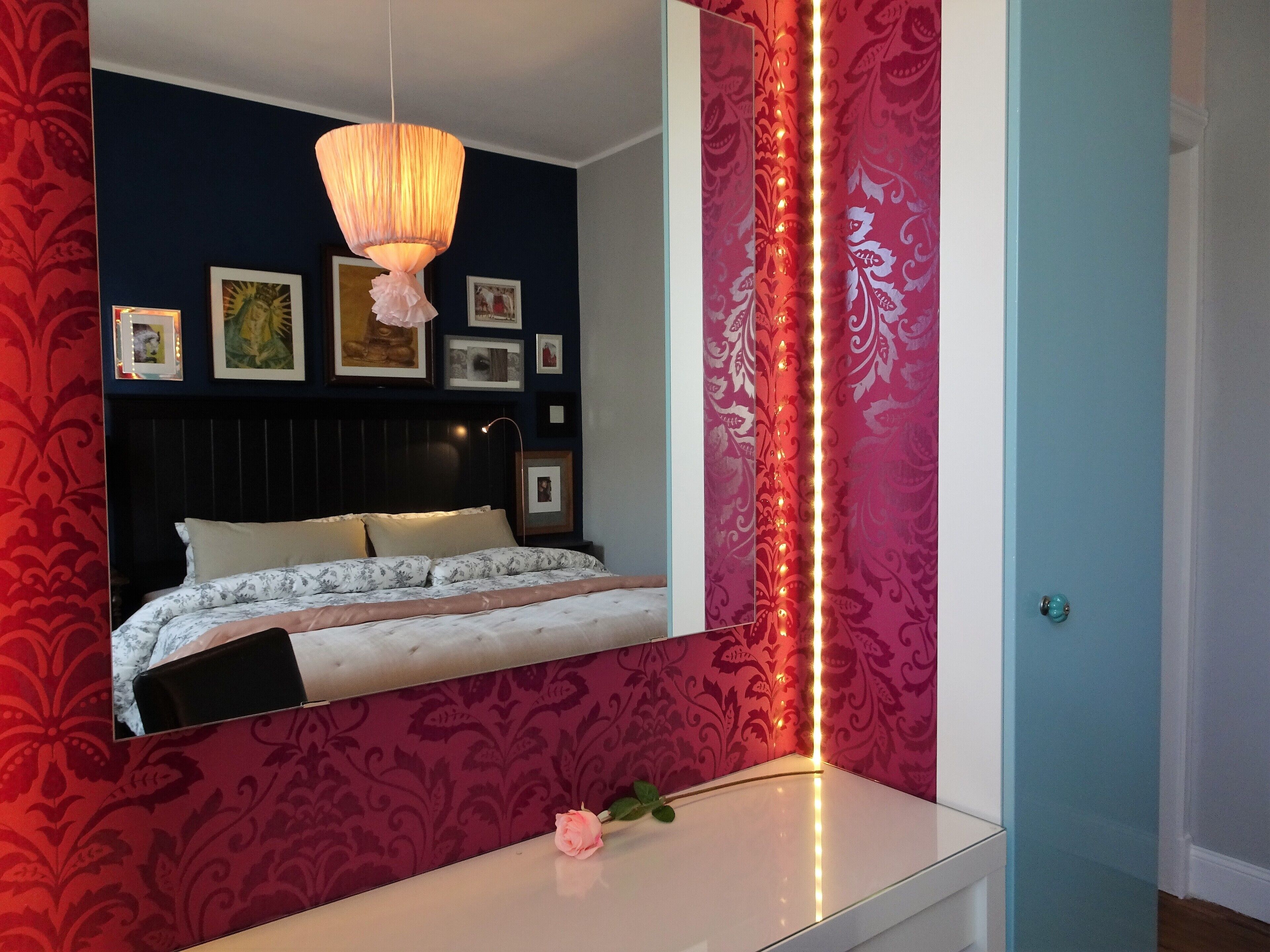 Un dormitorio con una cama, una mesita de noche, un espejo y un papel tapiz con diseño.