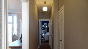 Un couloir étroit avec un plancher en bois, des murs blancs et un luminaire au plafond.